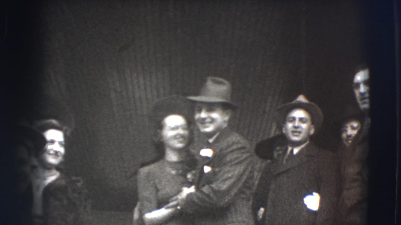 Smiling adults in formal clothing stand close together outside, with a man and woman near the center.