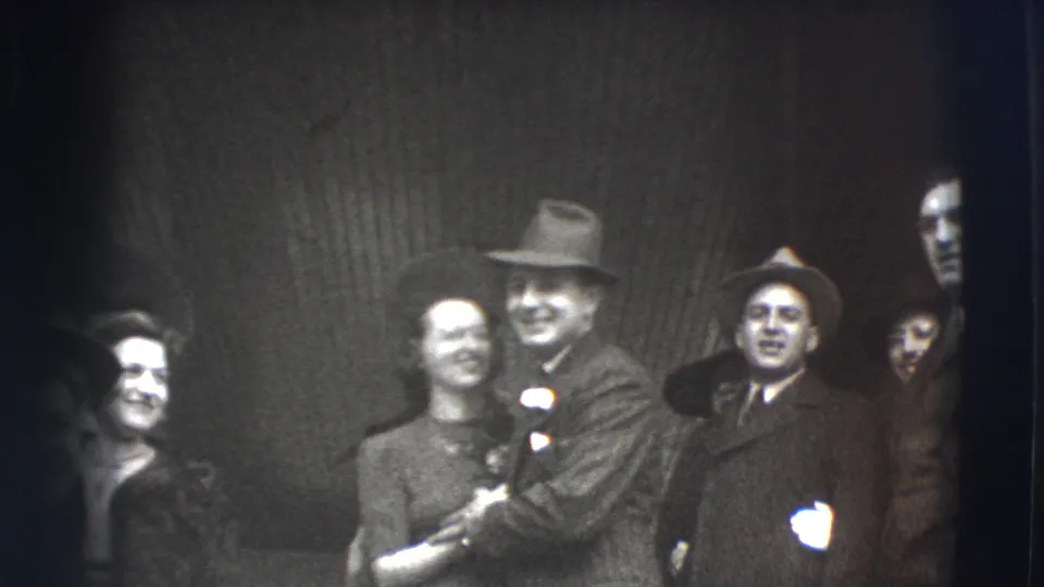 In 1941 Joliet home-movie footage, formally dressed adults smile toward the camera, with a couple near the center and other guests nearby.