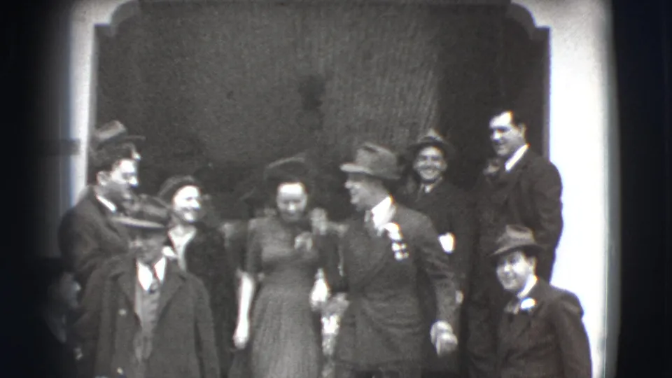 The Joliet, Illinois 8mm frame shows a group in 1940s formal clothing gathered on steps near a doorway or wall.