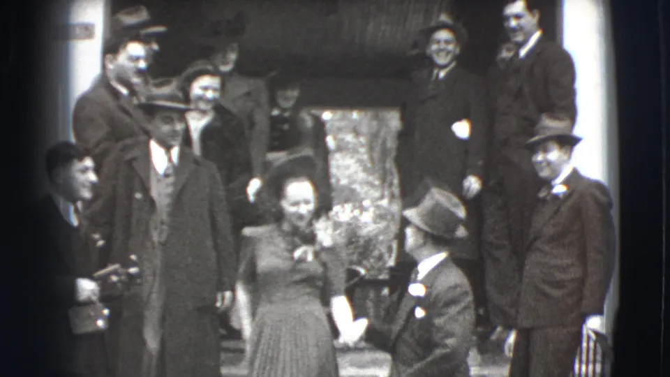 Formally dressed adults in 1941 Joliet appear on exterior steps, some smiling at the camera while others turn toward each other.