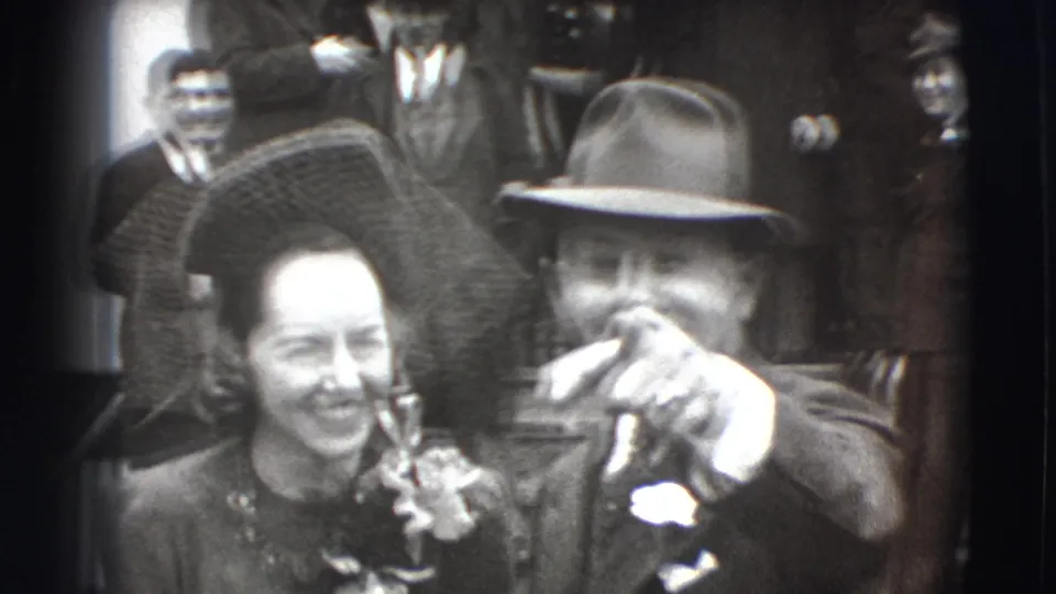 The wedding couple in Joliet, Illinois, appears close to the camera, with the man in a fedora pointing while the woman smiles.