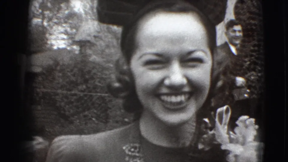A close 1941 home-movie view shows the smiling bride or wedding guest holding flowers, with people gathered behind her outdoors.