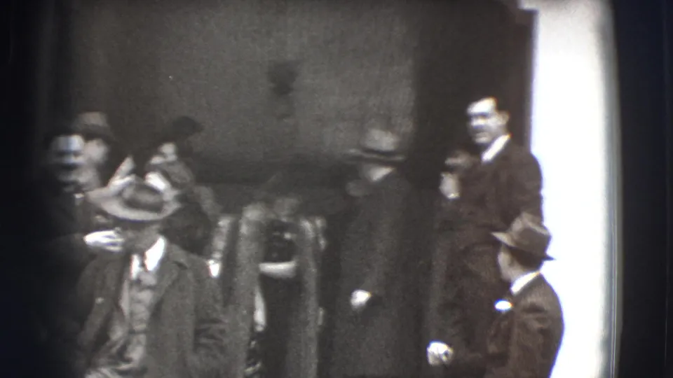In 1941 Joliet home-movie footage, adults in formal coats and hats shift and descend outside a chapel-like entrance.