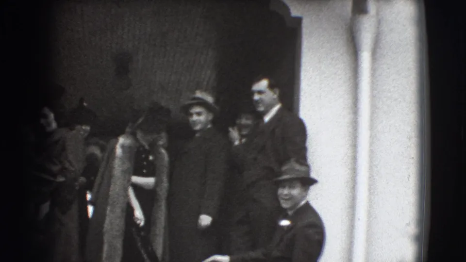 A woman in a fur coat and hat walks down exterior steps among suited men in Joliet, Illinois, 1941 home-movie footage.