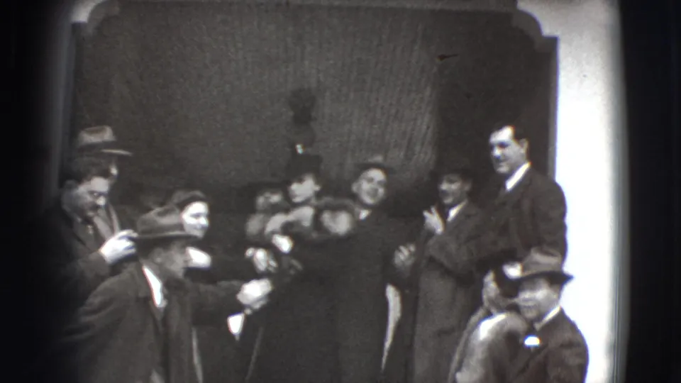 Joliet, Illinois 1941 home-movie frame showing formally dressed guests clustered in a doorway while men in hats stand in the foreground.