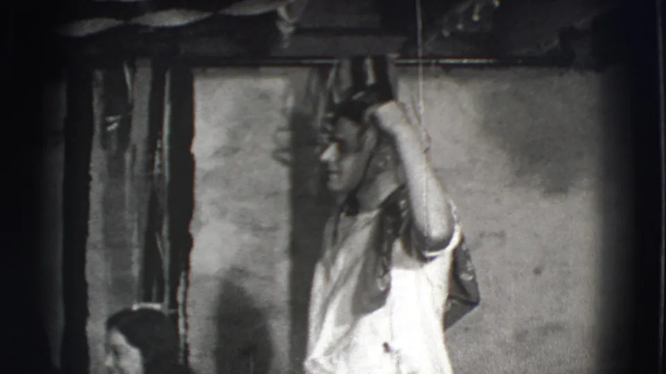Joliet 1941 home-movie frame showing a man in profile, wearing a white shirt and tie, gesturing beside a plain indoor wall.