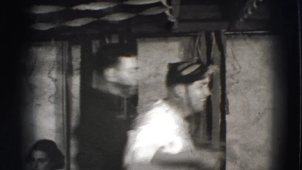 A male performer in a white shirt is seen in profile inside a private Joliet interior, with soft 8mm blur and high contrast.