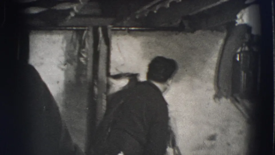 An adult man in dark clothing turns away in the rustic private interior as the brief home-movie performance continues.