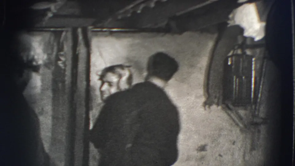 Joliet, Illinois 1941 home-movie frame showing adult men in a dim basement, with one figure turned toward a man near the wall.