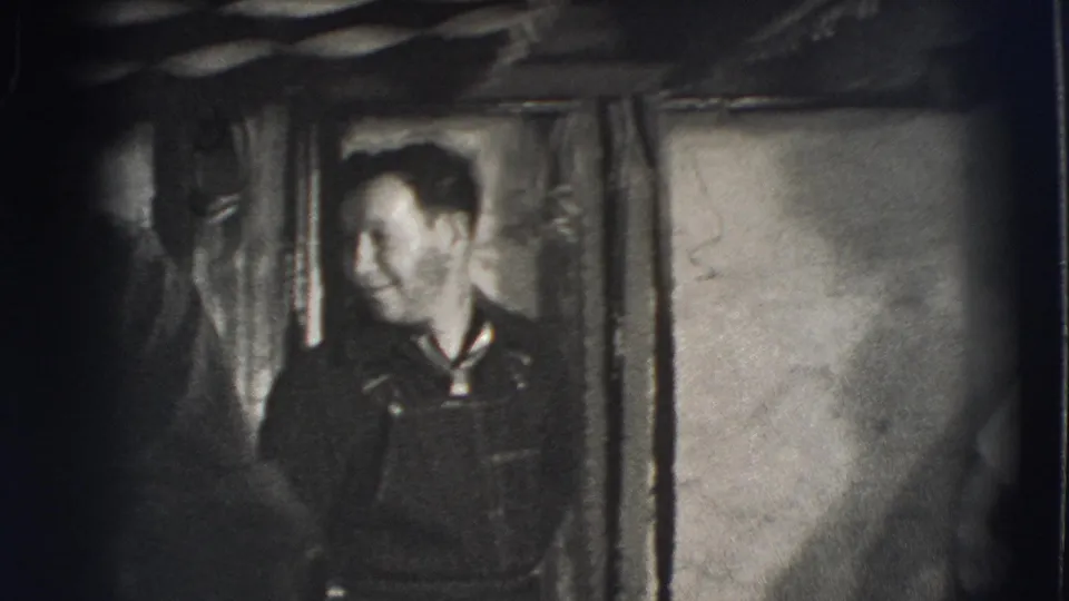 Joliet, Illinois 1941 frame showing an adult man in overalls smiling near a doorway in the dim private basement interior.