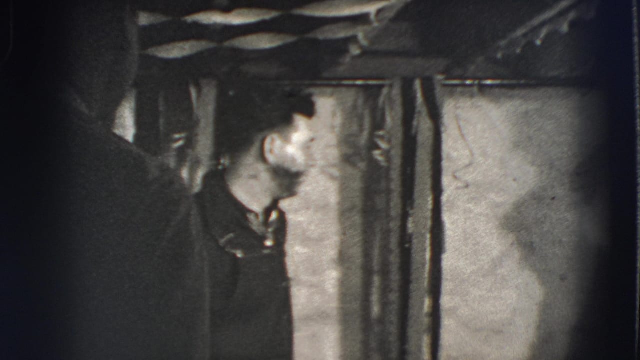 Man in dark clothing stands beside draped curtains on a small indoor stage.