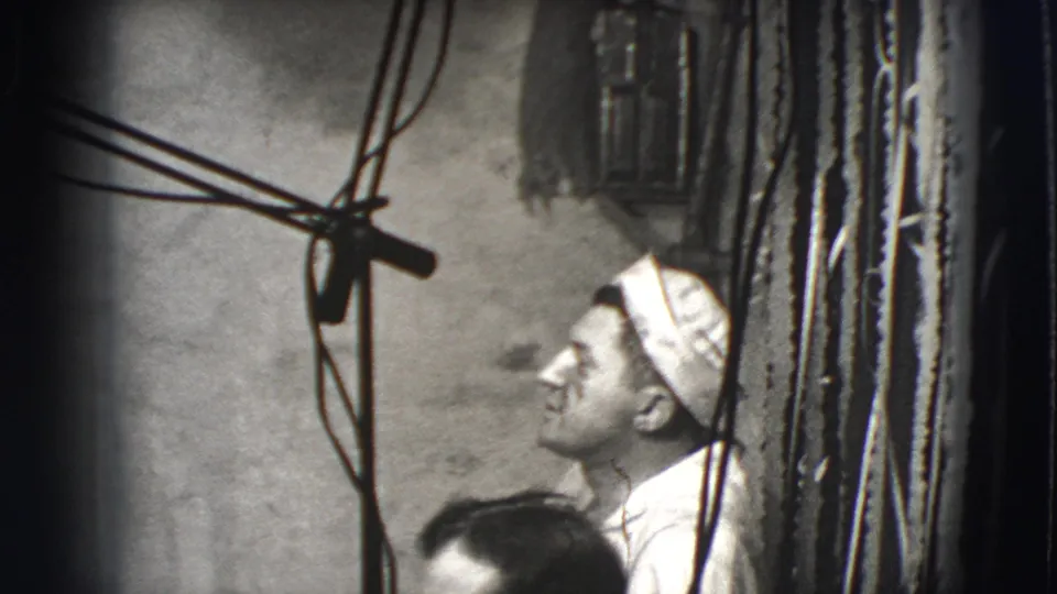 1941 Joliet frame showing a man in a white cap looking upward near exposed wires and a rough interior wall.