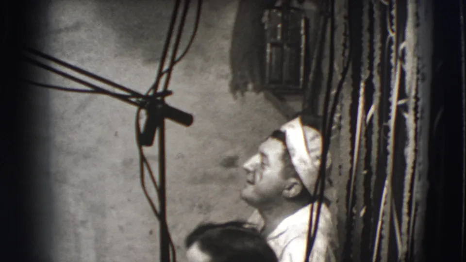 1941 Joliet home-movie frame with a man in a white cap looking upward beneath visible wires, with another person partly in front.
