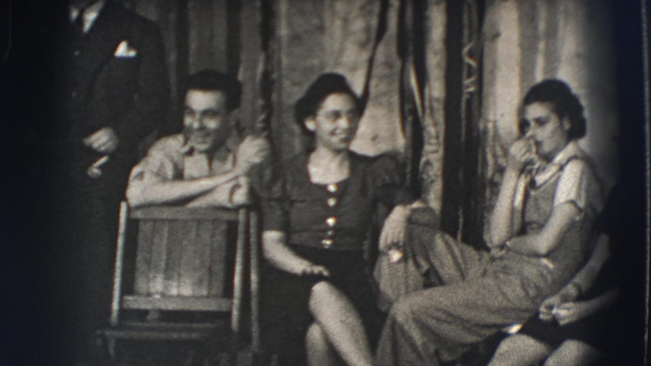 Three seated young adults laugh in a dim room while a man stands partly visible at left.