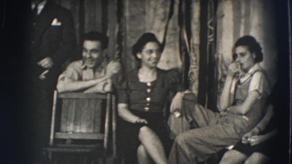 Joliet, Illinois, 1941 home-movie frame of young adults seated by wooden chairs and draped fabric as a partly seen man stands nearby.
