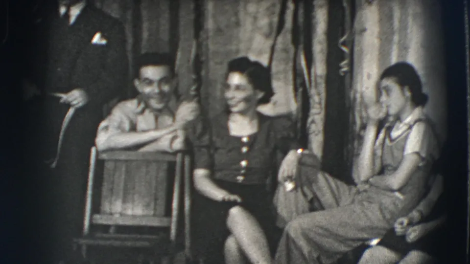 Joliet, Illinois, 1941 frame showing a man holding a cane beside seated young adults in a dim room with fabric decorations.