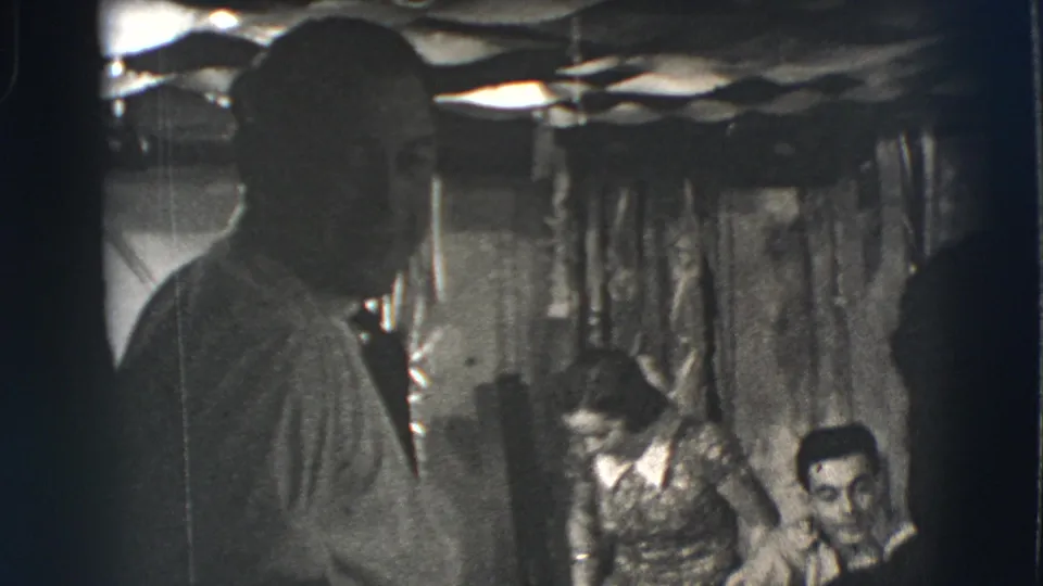 Joliet, Illinois, 1941 home-movie frame with a dark foreground figure and seated adults partly visible against a draped interior wall.