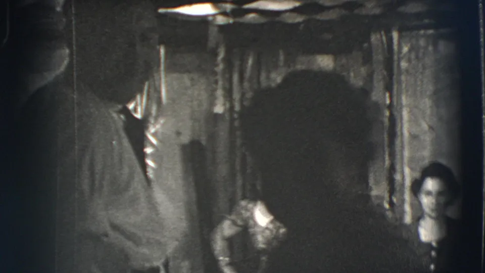 Joliet, Illinois, 1941 frame with shadowed foreground figures, a seated woman at right, and draped fabric in a small interior space.