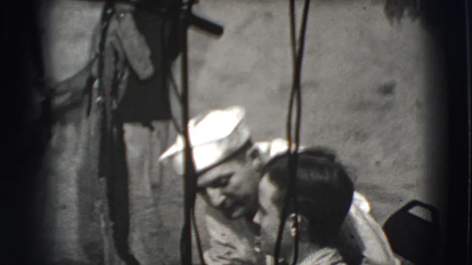 1941 Joliet frame with a sailor-capped man smiling or speaking close to another man in a shadowed interior with hanging straps.