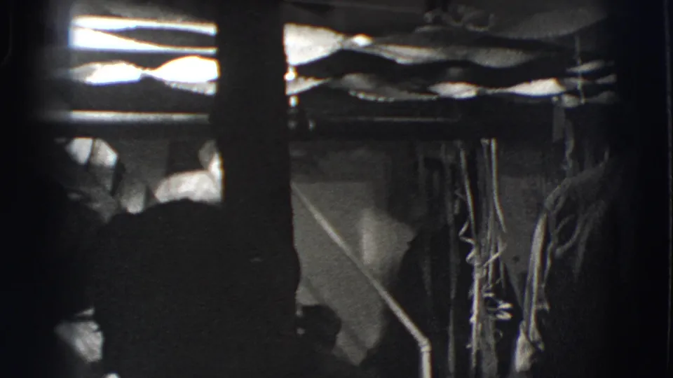 Black-and-white 1941 home-movie frame showing a dark, cramped interior with bunk-like framing, fabric, and partial figures.