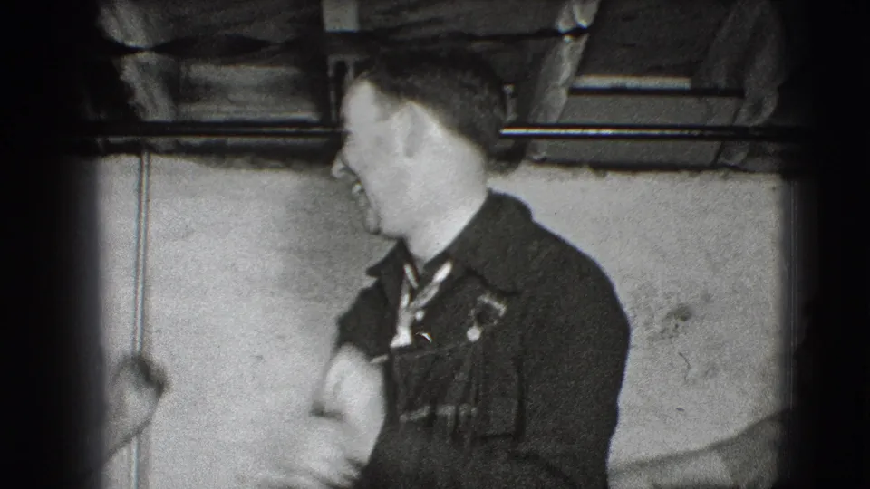 An adult man in a dark jacket turns in profile during playful movement inside the Joliet private interior.