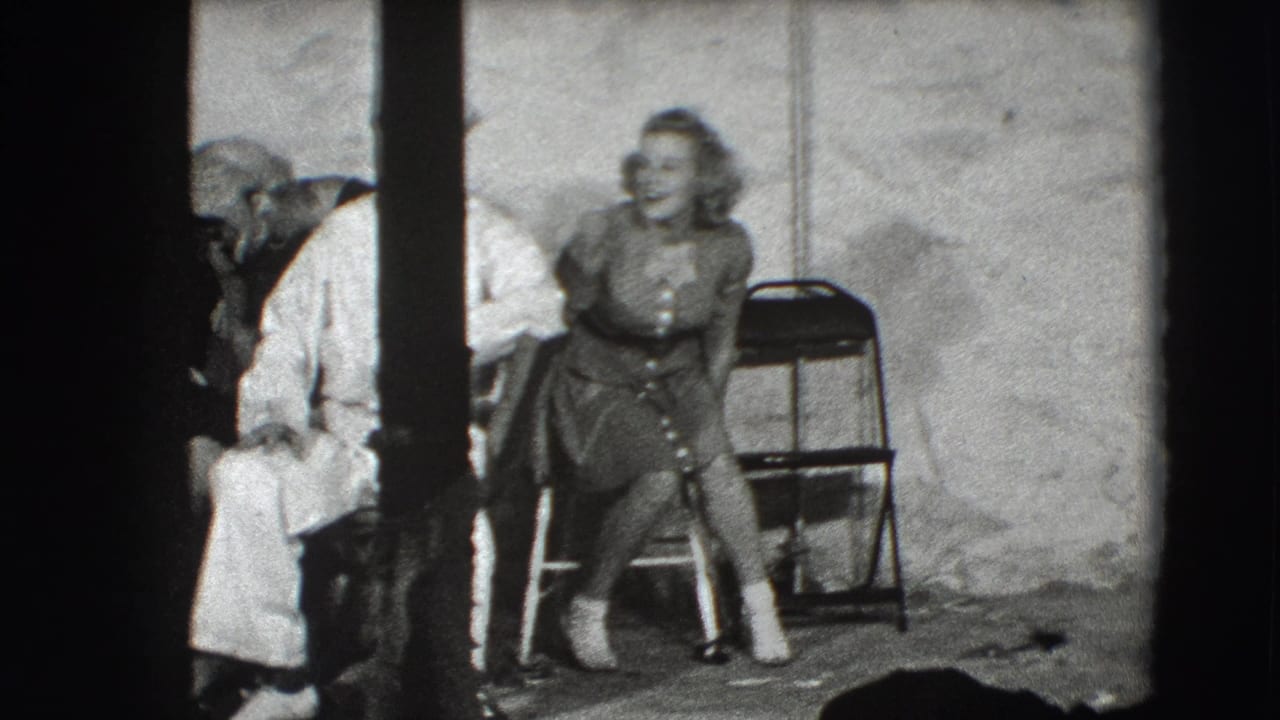 In 1941 Joliet, Illinois footage, a young woman sits on a folding chair as sailors in white uniforms stand close by in a studio setting.