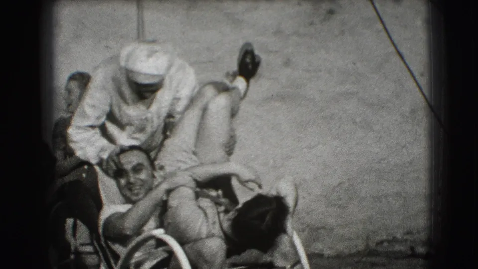 The 1941 Joliet home movie shows the capped man bending over the seated man in the wheelchair while the group stays gathered.