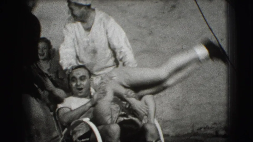 In 1941 Joliet home-movie footage, a sailor in white lifts a woman as nearby adults react against a wall or bulkhead.