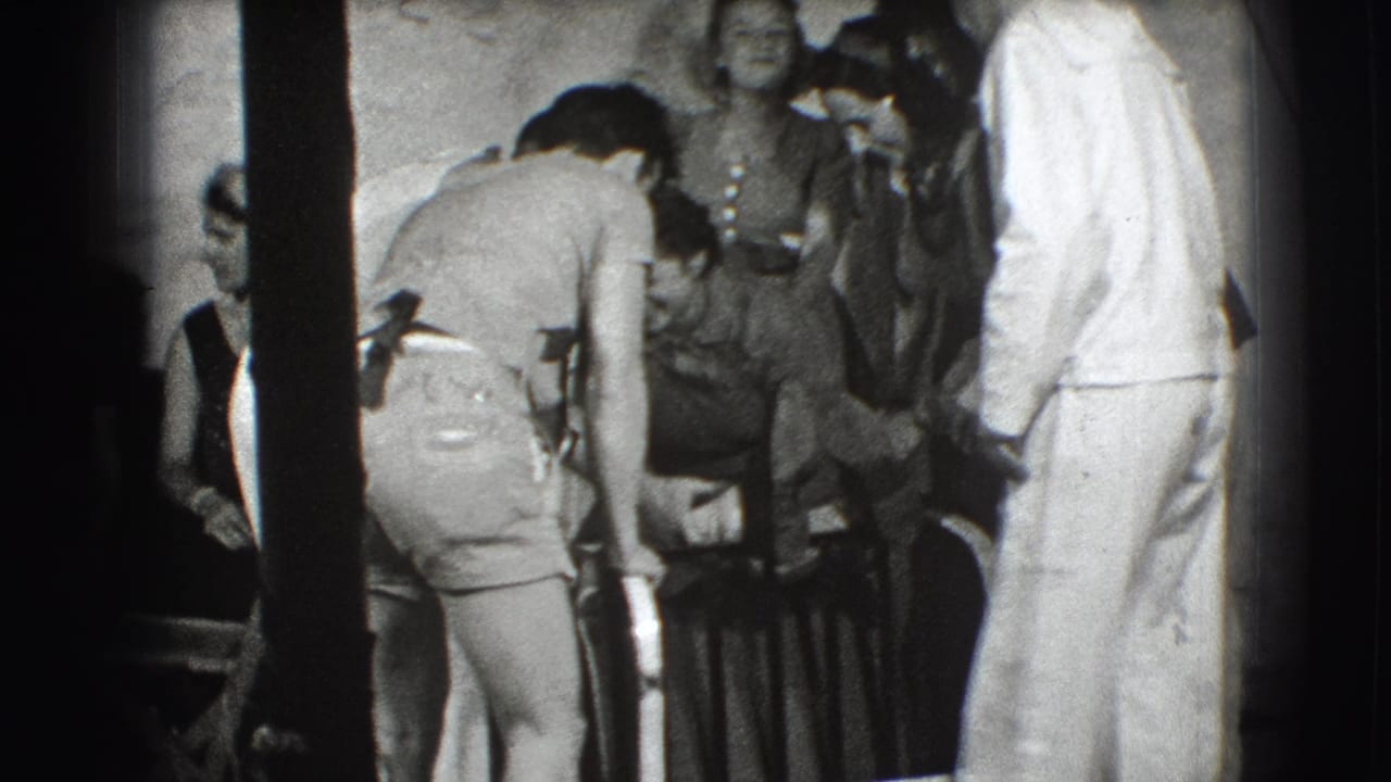 People gather indoors while a man bends near a curved metal object.