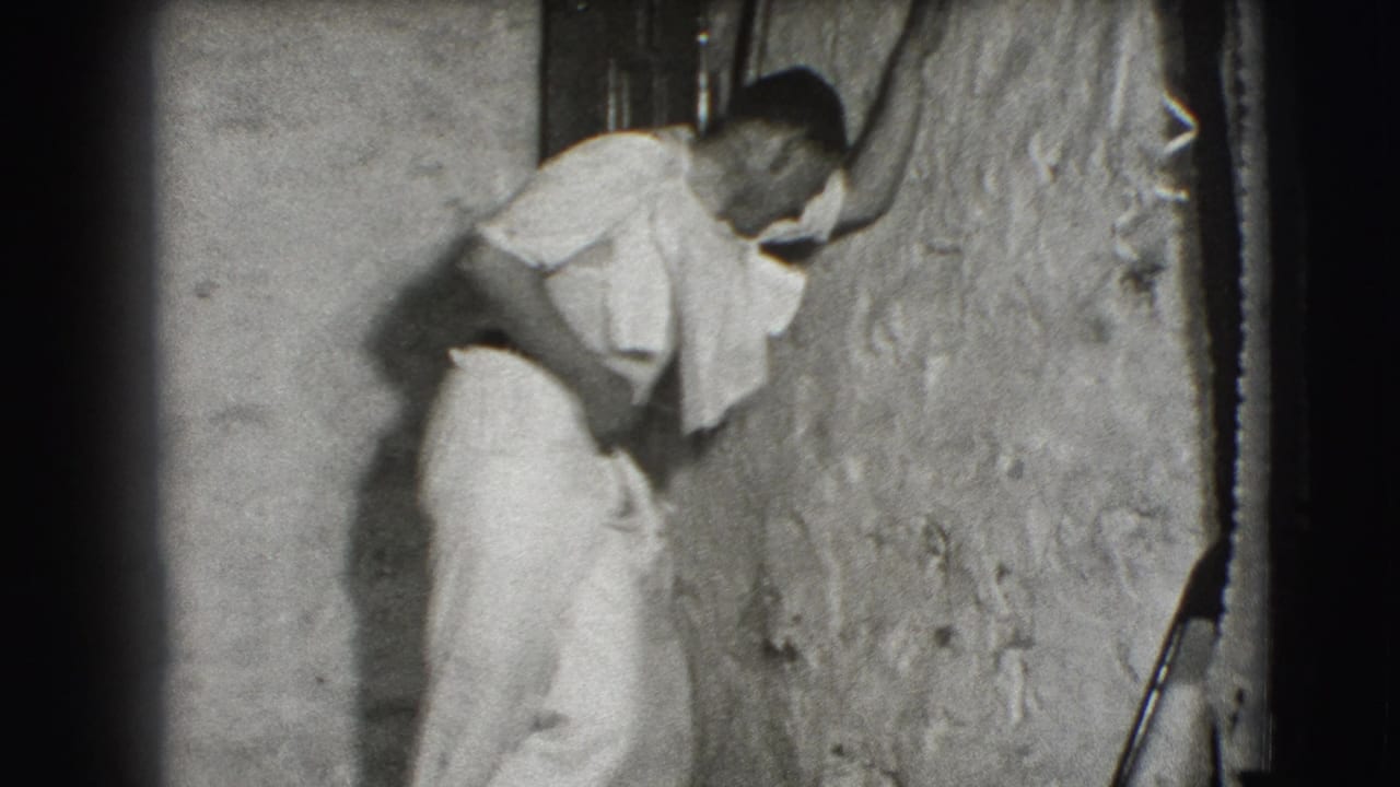 Man in light clothing leaning against a rough wall.
