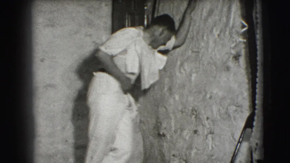 A man in light clothing appears to lean into or against a rough interior wall in the 1941 Joliet, Illinois home-movie scene.