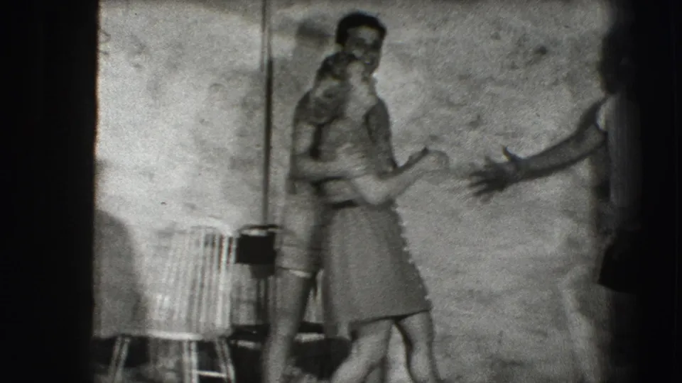 A couple appears to embrace or laugh near a rough wall, with another adult's arm entering from the side in the 1941 Joliet, Illinois home-movie footage.