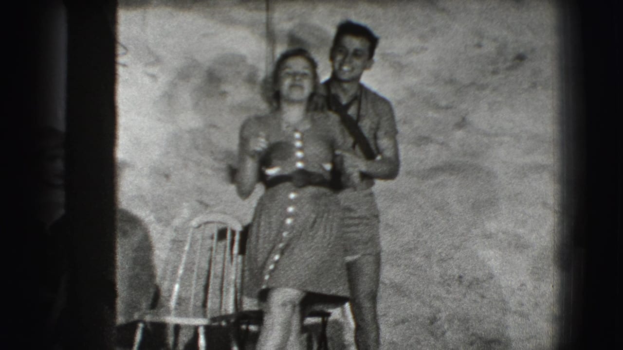 Woman in a button-front dress smiles as a man stands behind her near a chair.