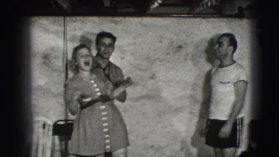 A smiling woman stands with a man behind her while another adult man watches nearby in the 1941 Joliet home-movie frame.