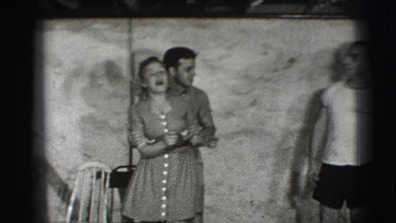 Woman in a patterned dress laughs beside a man as another person stands near a plain wall.