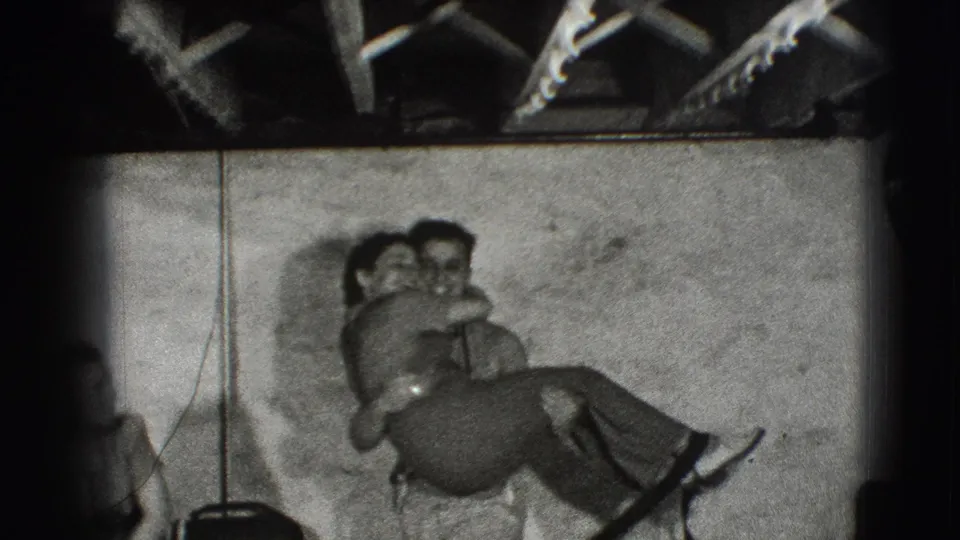 In listed 1941 Joliet home-movie footage, a young couple holds each other closely inside a plain room with exposed beams overhead.