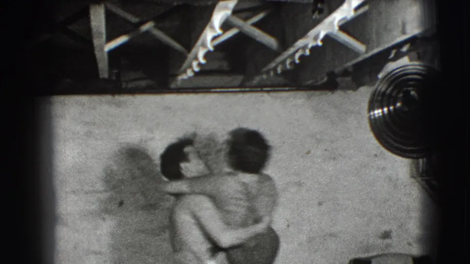 In the supported 1941 Joliet setting, the couple kisses while one partner lifts or carries the other in a sparse interior.