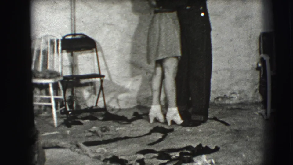 A cropped view shows the couple pressed close in the Joliet interior, with folding chairs, white heels, and the rough floor covering visible.