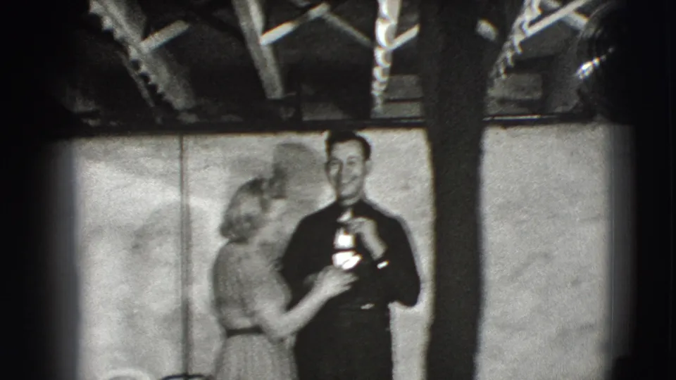 A woman faces a man in dark clothing who appears to hold a bottle-shaped object in the same 1941 Joliet interior.