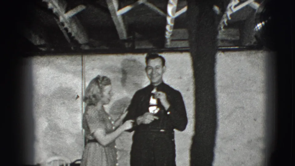 The woman stands beside the man in the 1941 Joliet interior, touching his arm while he faces the camera.