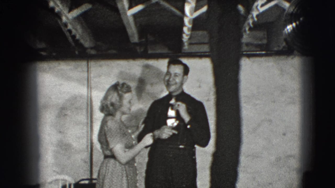 Woman in a light dress presents a small object to a smiling man in a dark suit indoors.