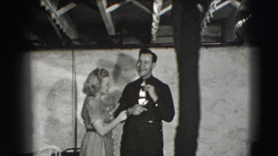 In 1941 Joliet home-movie footage, a woman in a light dress appears to hand a small award or gift to a smiling man indoors.