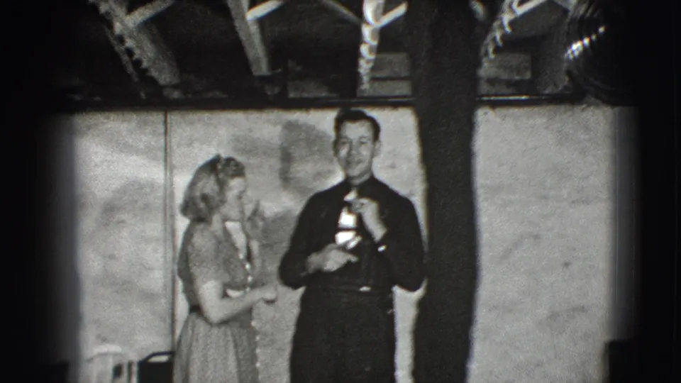 The woman stands close to the man as he holds the small presentation object in a black-and-white 1941 Joliet indoor scene.