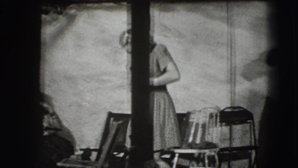 At the end of the 1941 Joliet clip, the woman remains near chairs while a dark vertical obstruction partly blocks the indoor scene.