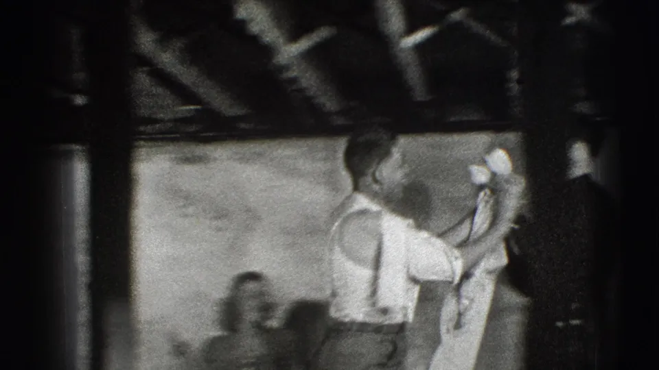 In a 1941 Joliet, Illinois home-movie frame, a man in a white shirt lifts or folds a light cloth in a basement-like room.