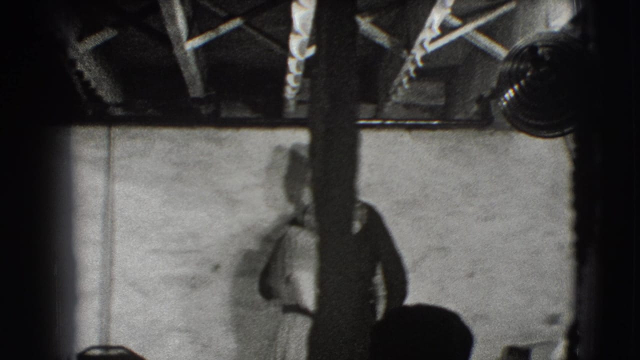 Man partly obscured by a post stands near studio lights in a dim interior.