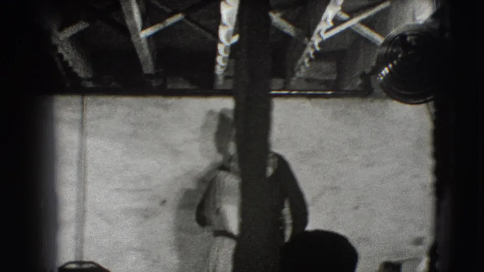 In the Joliet 1941 footage, a man stands near a plain wall while overhead beams and studio lamps frame the dim interior.