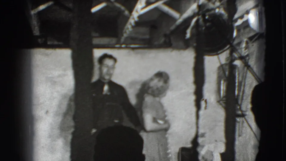 A man in dark clothing and a woman in a light dress stand together under visible studio lighting in the Joliet 1941 interior.