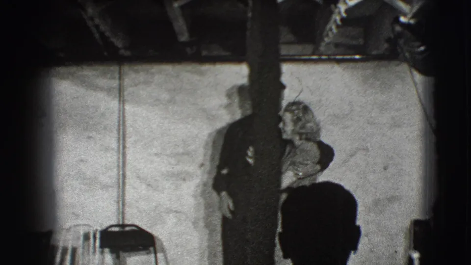 In metadata-supported 1941 Joliet footage, an adult couple stands indoors facing the camera with a post partly blocking the view.