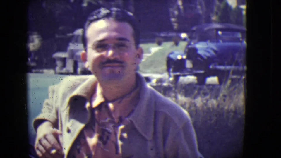 Smiling adult man outdoors in East Orange, New Jersey, 1946, with vintage automobiles behind him.